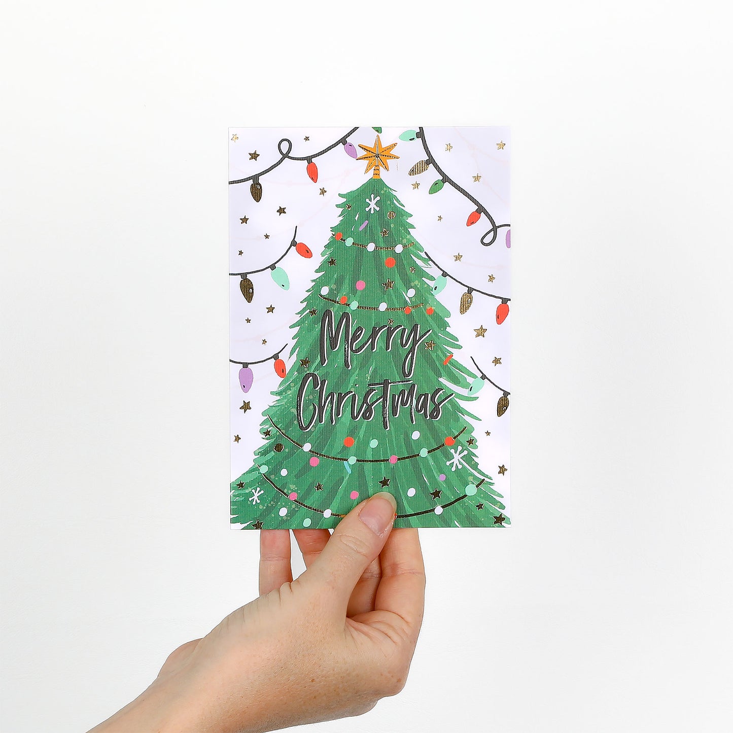 Hand holding a Christmas card with a green tree and 'Merry Christmas' text on a white background