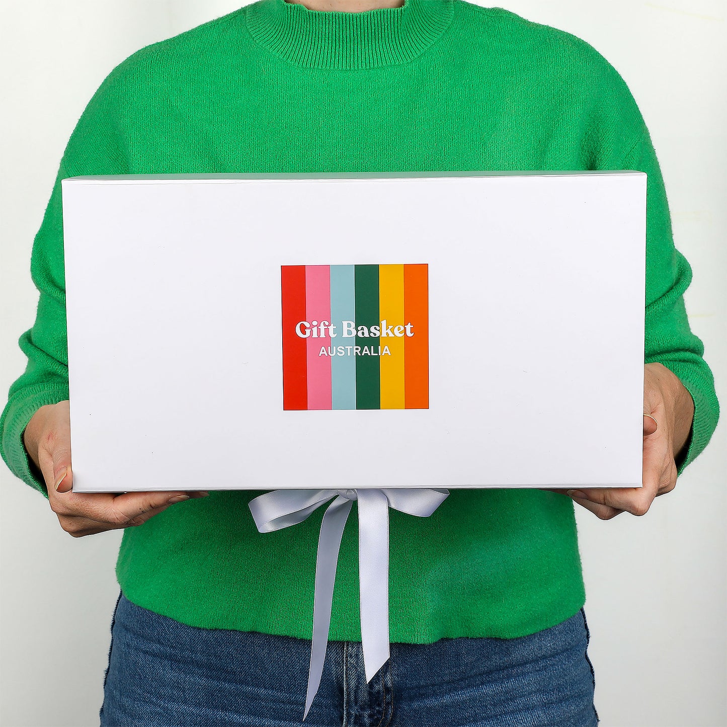Person holding a white gift box with colorful Gift Basket Australia label against a plain background