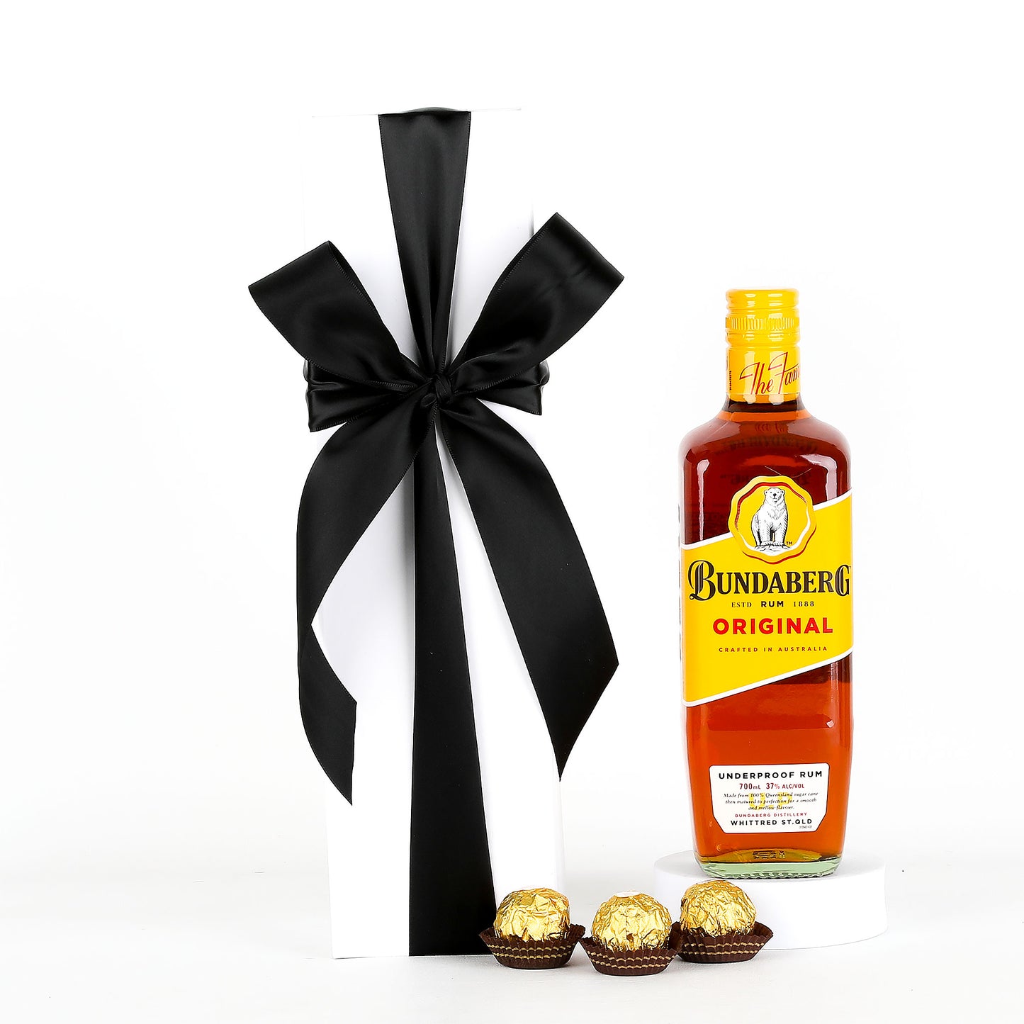 Bottle of Bundaberg rum with a black ribbon and gold wrapped chocolates on a white background