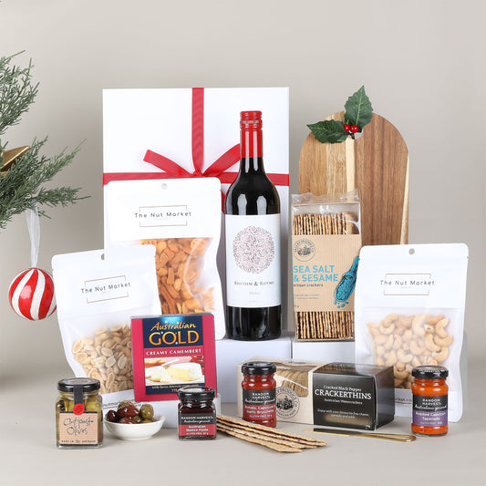 Gourmet gift basket with wine, snacks, and condiments on a neutral background