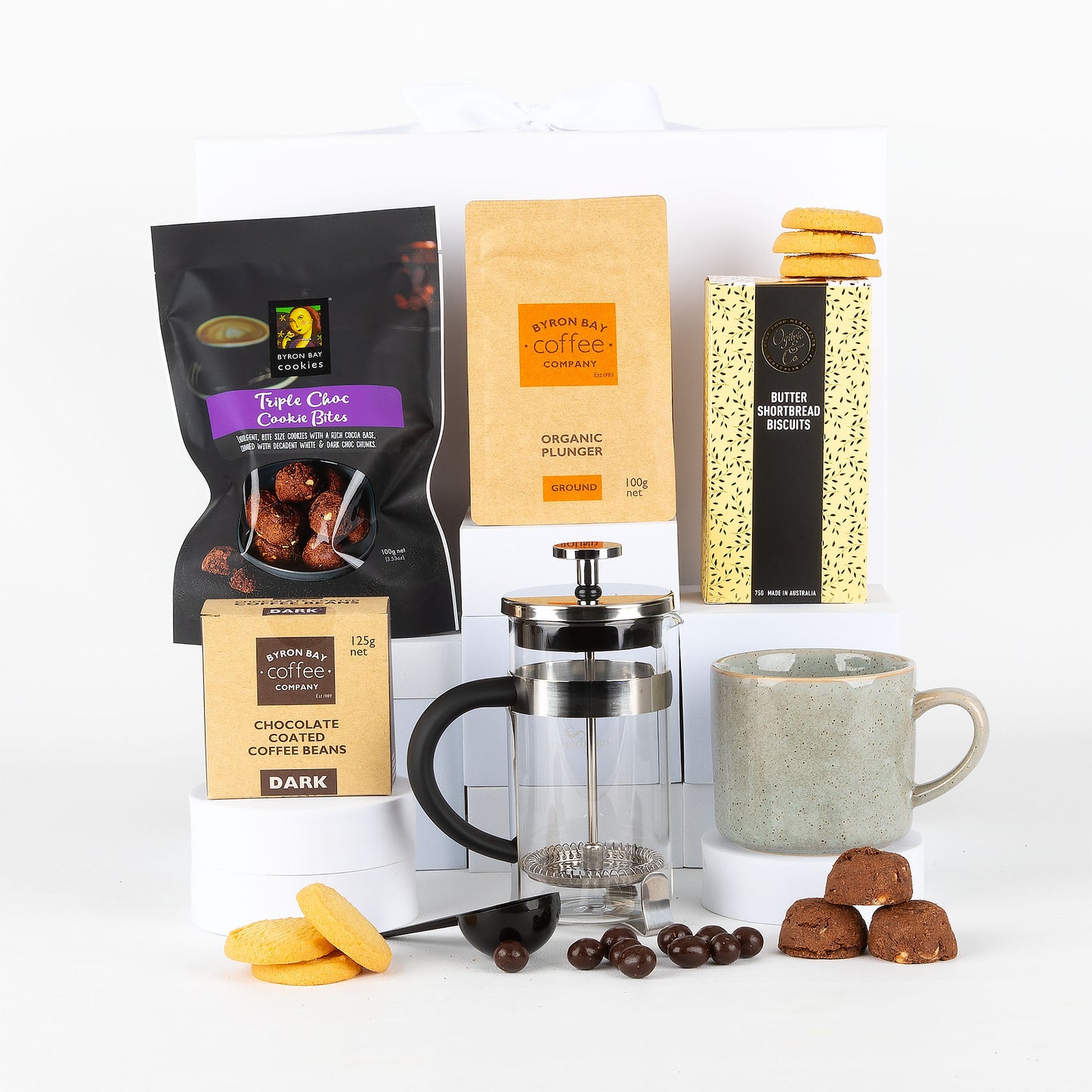 Collection of coffee products including mug, plunger, and cookies on a white background