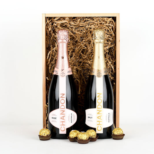 Two bottles of Chandon champagne in a wooden gift box with chocolates on a white background