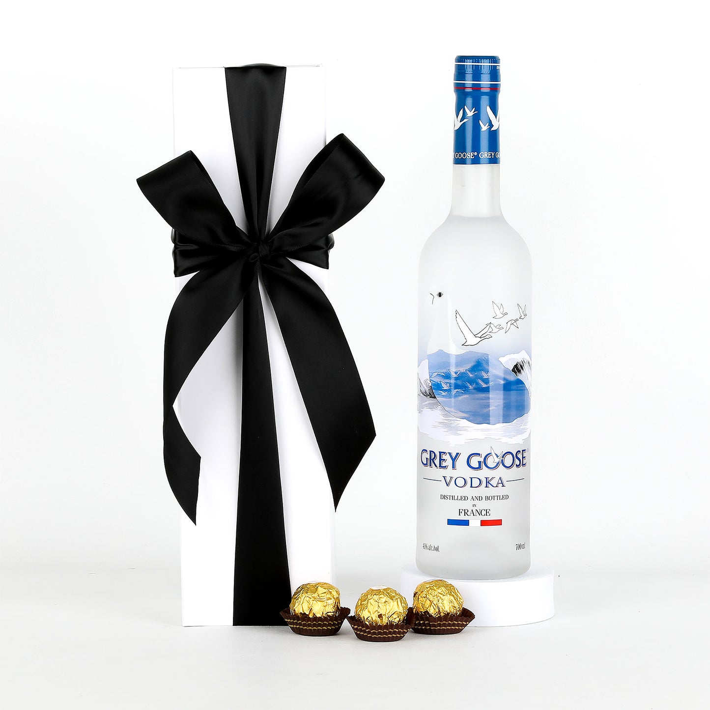 Grey Goose vodka bottle with a black bow and Ferrero Rocher chocolates on a white background