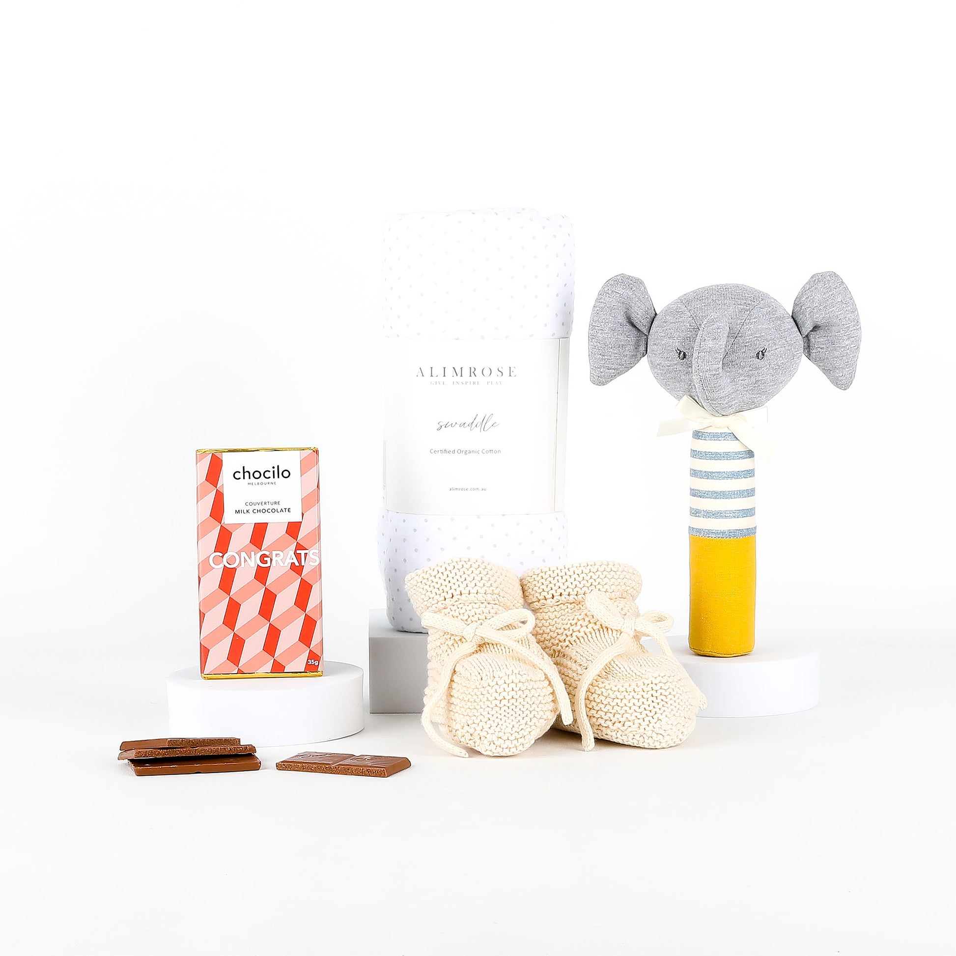 Baby booties, chocolates, and elephant rattle on a white background