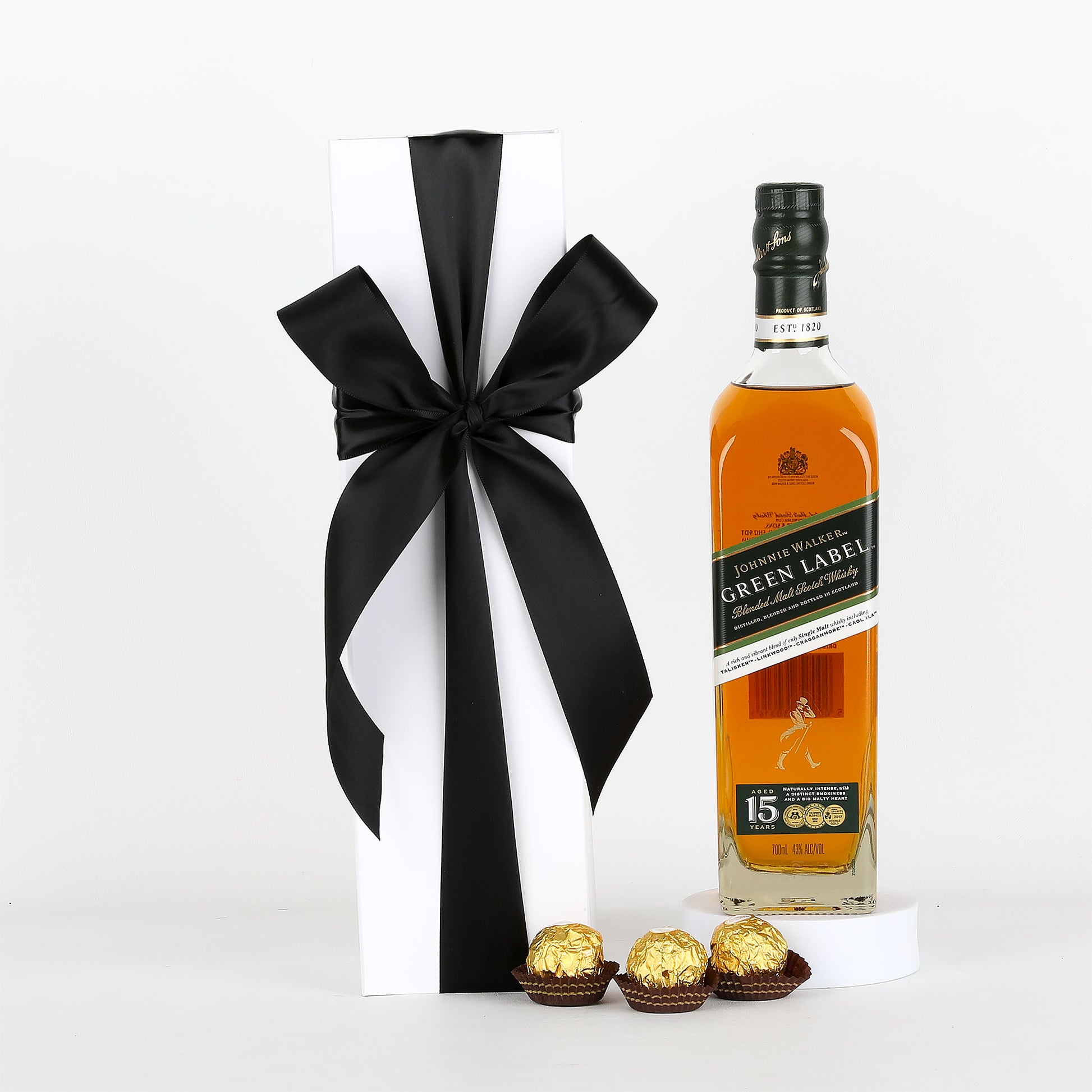 Johnnie Walker Green Label whisky bottle with a black ribbon and Ferrero Rocher chocolates on a white background