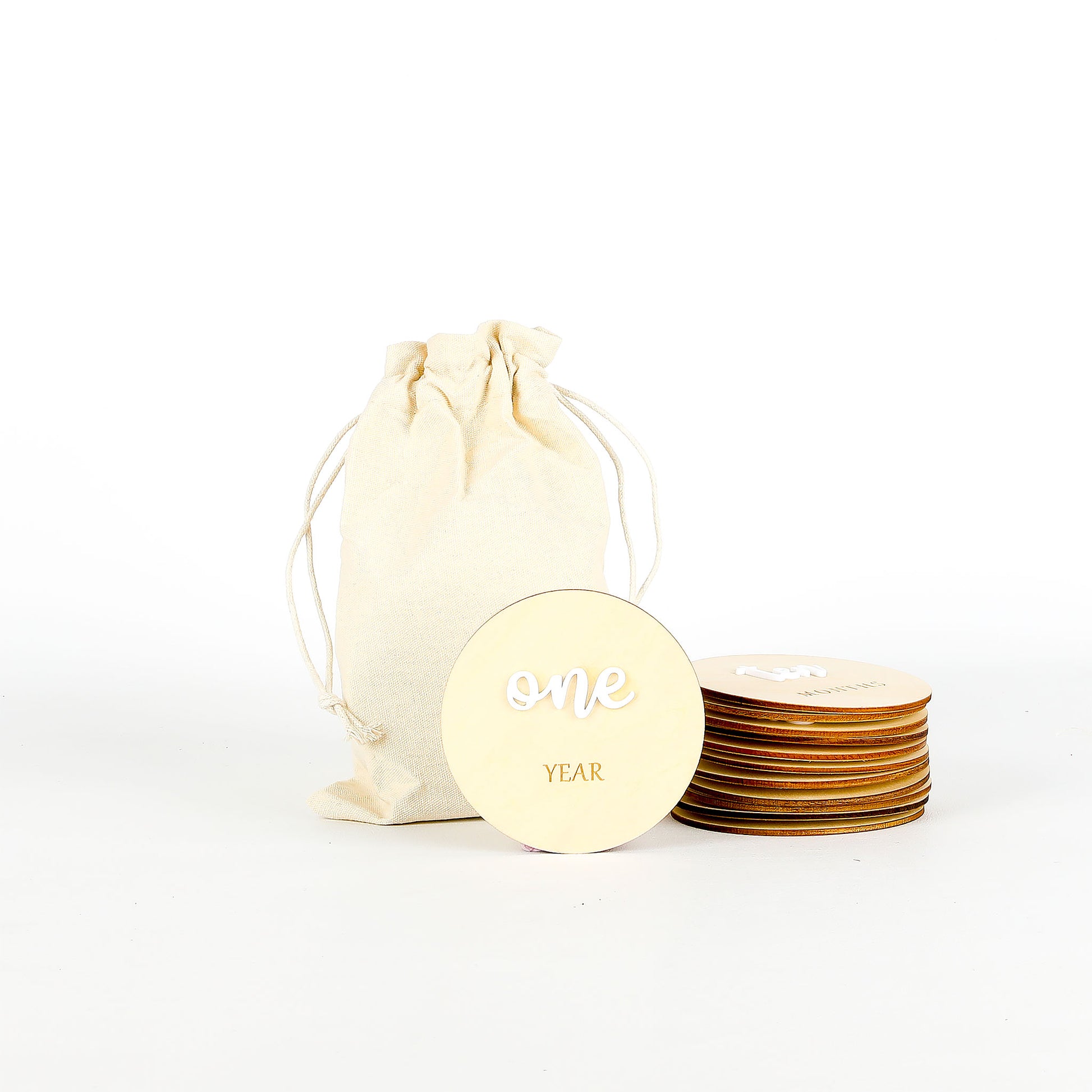 Wooden milestone discs placed next to a cream-colored drawstring bag on a white background