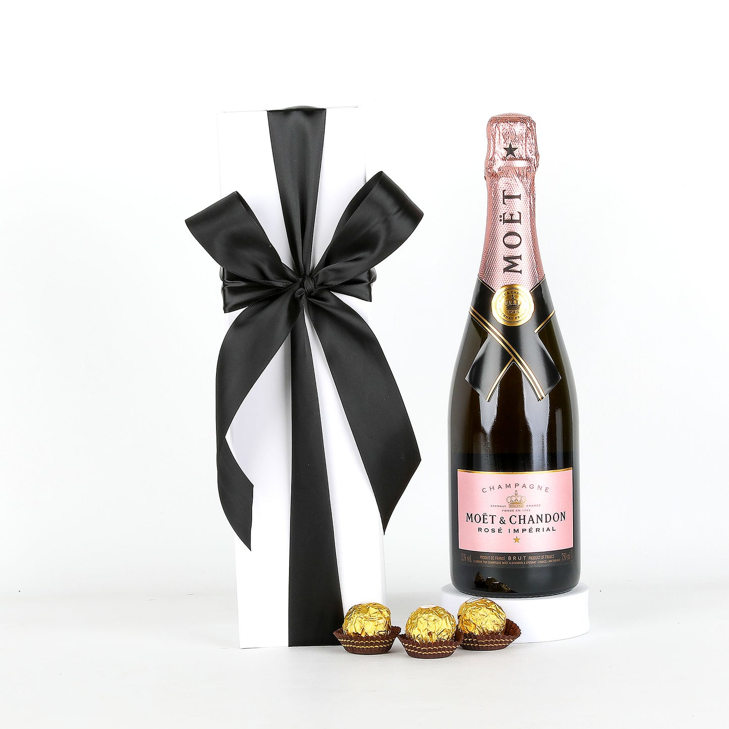Bottle of Moët & Chandon champagne with a black ribbon and Ferrero Rocher chocolates on a white background