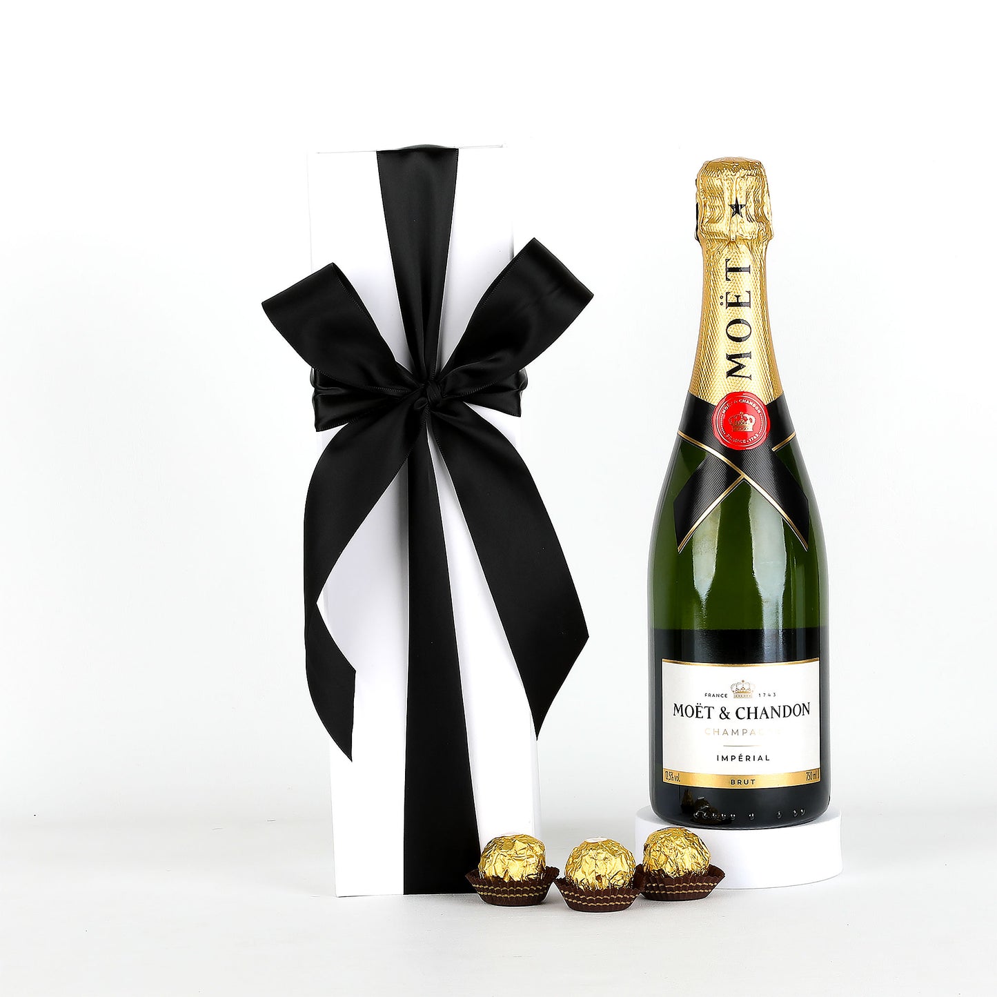 Moët & Chandon champagne bottle with a black bow and gold chocolates on a white background
