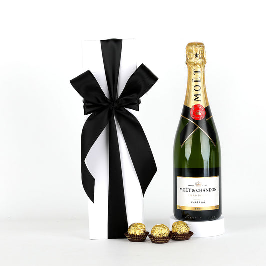 Moët & Chandon champagne bottle with a black bow and gold chocolates on a white background