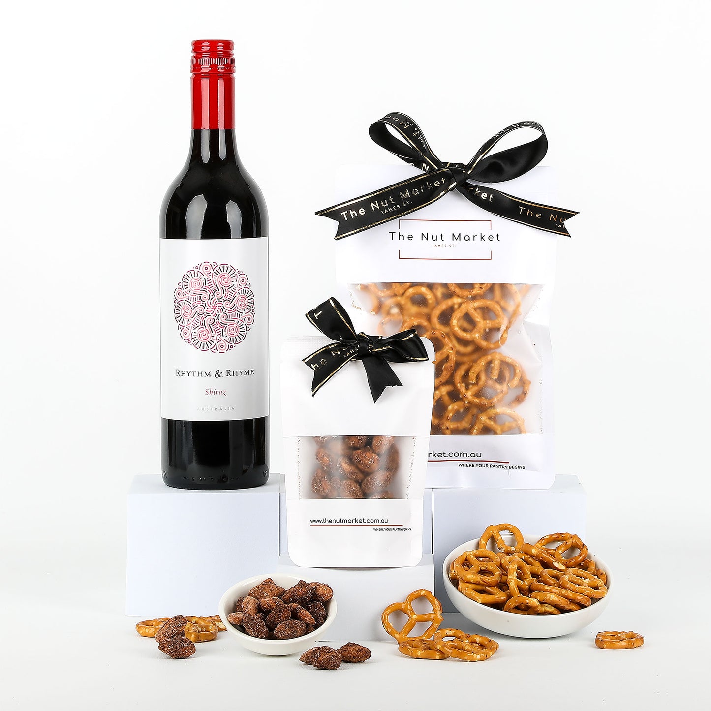 Bottle of red wine with crunchy salted pretzels and caramelised nuts on a white background