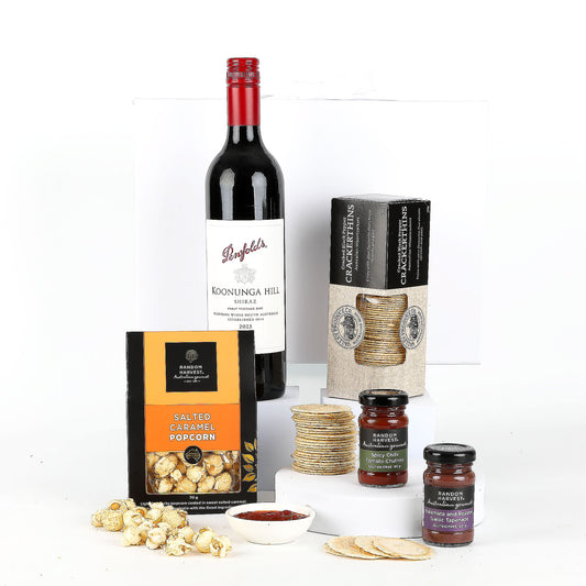 Penfolds wine bottle with popcorn, crackers, and chutney on a white background