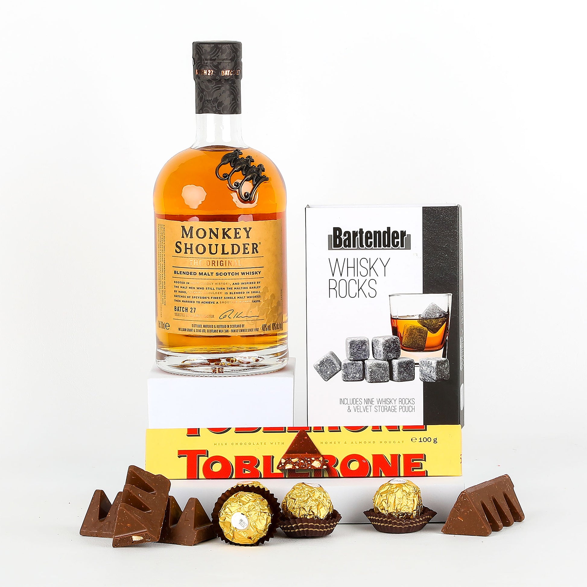 Bottle of Monkey Shoulder whisky with a box of whisky rocks and Toblerone chocolate on a white background