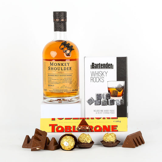 Bottle of Monkey Shoulder whisky with a box of whisky rocks and Toblerone chocolate on a white background